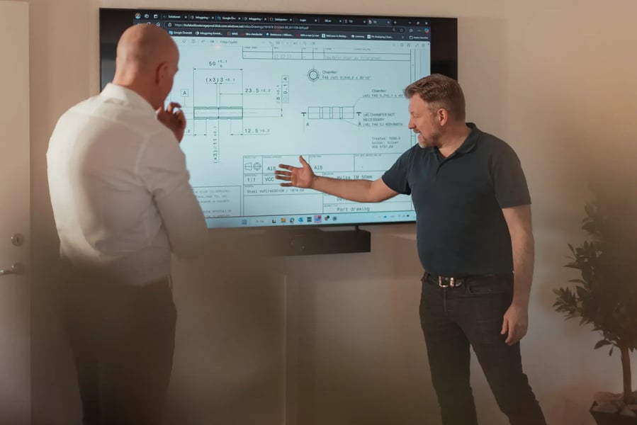 Two men in front of a large screen with a detailed drawing